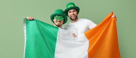 Photo for Happy young men in leprechaun's hats and with flag of Ireland on green background. St. Patrick's Day celebration - Royalty Free Image