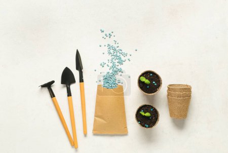 Téléchargez les photos : Outils de jardinage, pots à tourbe et sac avec engrais granulaire bleu sur fond blanc - en image libre de droit