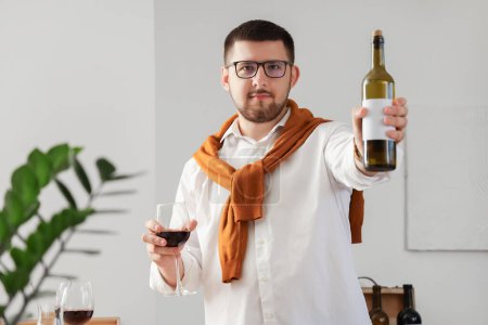 Photo for Young sommelier with bottle and glass of wine in kitchen at home - Royalty Free Image