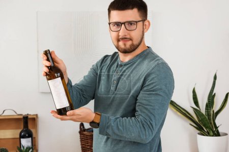 Young sommelier with bottle of wine in kitchen at home