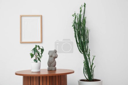 Foto de Gran cactus con mesa y decoración casera cerca de la pared blanca en la habitación - Imagen libre de derechos