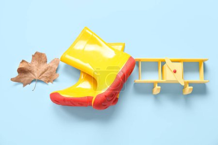 Foto de Botas de goma amarillas con avión de juguete y hoja de otoño sobre fondo azul - Imagen libre de derechos