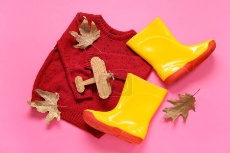 Foto de Botas de goma amarillas con suéter, avión de juguete y hojas de otoño sobre fondo rosa - Imagen libre de derechos