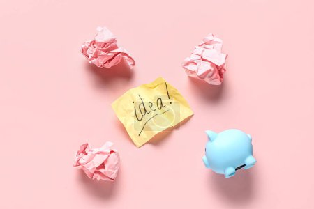Foto de Papel arrugado, alcancía y hoja con palabra IDEA sobre fondo rosa. Concepto de idea empresarial - Imagen libre de derechos