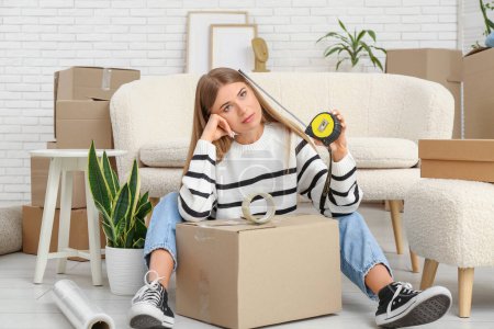 Foto de Mujer joven cansada con caja de cartón, adhesivo y cintas métricas en la sala de estar. Mudanza concepto casa - Imagen libre de derechos