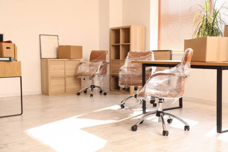 Téléchargez les photos : Intérieur du bureau léger avec des chaises enveloppées dans un film étirable et des boîtes en carton le jour du déménagement - en image libre de droit