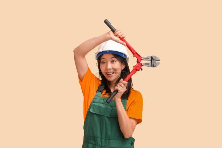 Photo for Asian woman in jumpsuit and hardhat with bolt cutter on beige background - Royalty Free Image