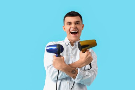 Photo for Handsome young man with hair dryers on blue background - Royalty Free Image