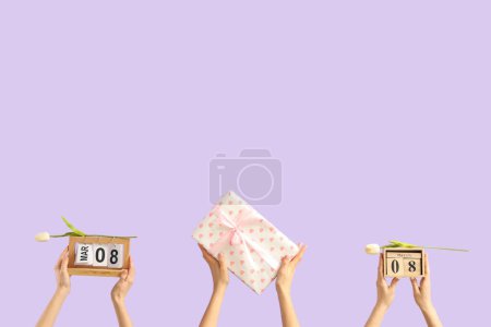Photo for Female hands with calendars, tulips and gift box on lilac background. International Women's Day celebration - Royalty Free Image