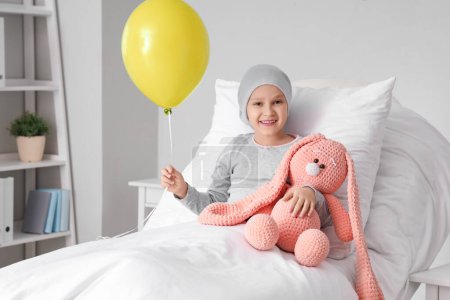 Téléchargez les photos : Petite fille après chimiothérapie avec ballon bleu et jouet couché à la clinique. Journée internationale du cancer chez les enfants - en image libre de droit