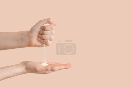 Photo for Female hands with pouring sand on beige background. Time concept - Royalty Free Image