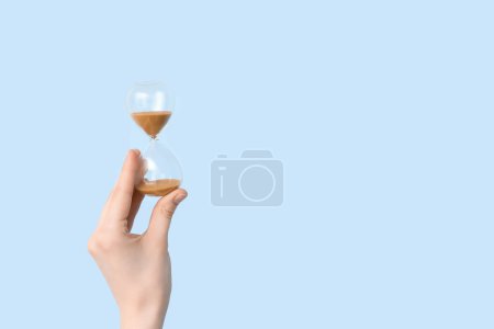 Photo for Female hand holding hourglass on blue background - Royalty Free Image