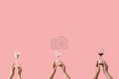 Photo for Female hands holding hourglasses on pink background - Royalty Free Image