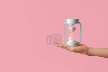 Photo for Female hand holding hourglass on pink background - Royalty Free Image