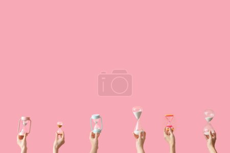 Photo for Female hands holding hourglasses on pink background - Royalty Free Image