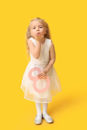 Téléchargez les photos : Petite fille mignonne avec la figure 8 en papier soufflant baiser sur fond jaune. Journée internationale de la femme - en image libre de droit
