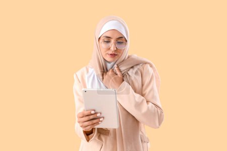 Junge Muslimin im schicken Anzug mit Tablet-Computer auf beigem Hintergrund