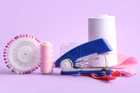Foto de Máquina de coser manual con carretes de rosca, pasadores de bolas y cremalleras sobre fondo lila - Imagen libre de derechos