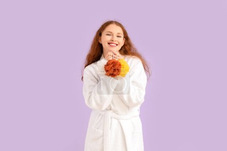 Foto de Mujer joven en albornoz con esponjas sobre fondo lila - Imagen libre de derechos