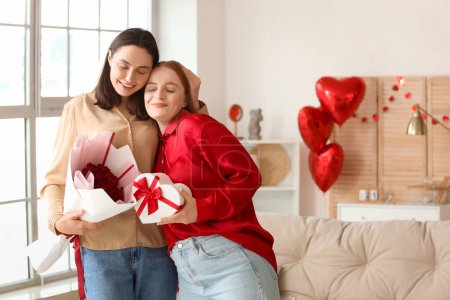 Young lesbian couple with gift and roses at home on Valentine's Day