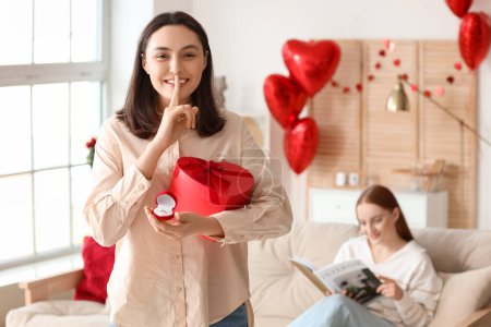 Jeune femme lesbienne avec cadeau et bague de fiançailles montrant un geste de silence à la maison le jour de la Saint-Valentin