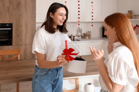 Jeune femme lesbienne saluant sa bien-aimée avec un cadeau dans la cuisine le jour de la Saint-Valentin