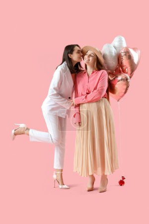 Jeune couple lesbien avec des ballons sur fond rose. Fête de la Saint-Valentin