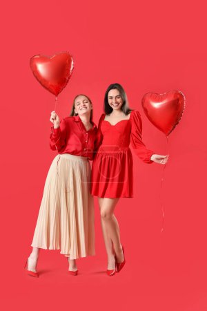 Young lesbian couple with heart-shaped balloons on red background. Valentine's Day celebration