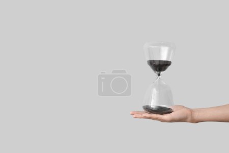 Female hand holding hourglass on grey background