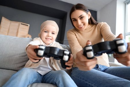 Téléchargez les photos : Petite fille après la chimiothérapie avec sa mère jouant à un jeu vidéo à la maison - en image libre de droit