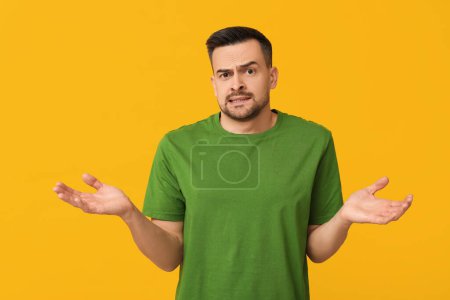 Handsome ashamed young man shrugging on yellow background