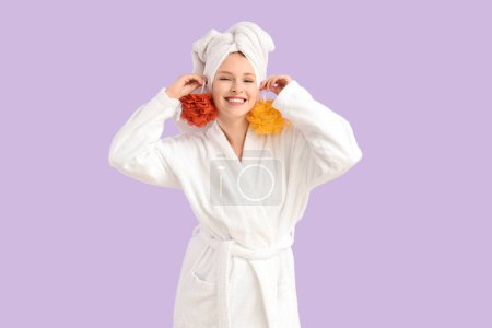 Foto de Mujer joven en albornoz con esponjas después de la ducha sobre fondo lila - Imagen libre de derechos