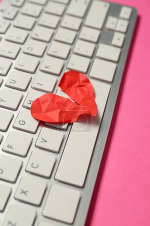 Computer keyboard and torn paper heart on pink background. Concept of online dating