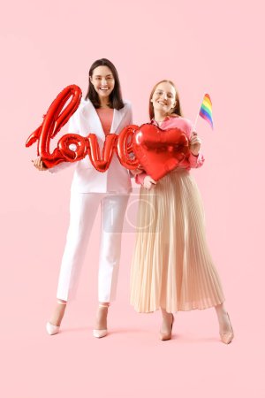 Jeune couple lesbien avec mot LOVE fait de ballons et drapeau LGBT sur fond rose. Fête de la Saint-Valentin