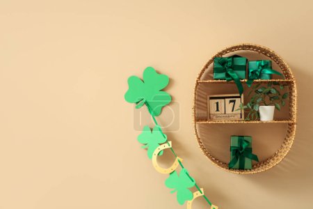 Wicker shelf with green gift boxes, clover, houseplant and cube calendar hanging on beige wall. St. Patrick's Day celebration