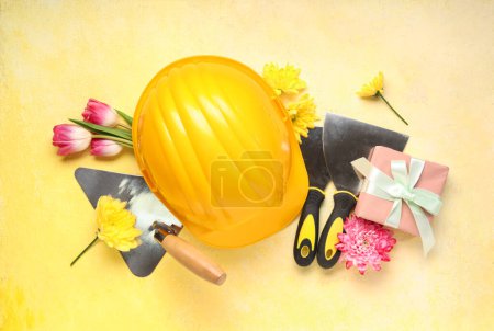 Composition with hardhat, building trowels and flowers on color background. International Women's Day