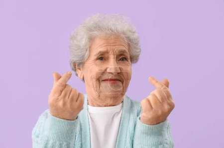 Femme âgée faisant c?ur avec ses doigts sur fond lilas, gros plan