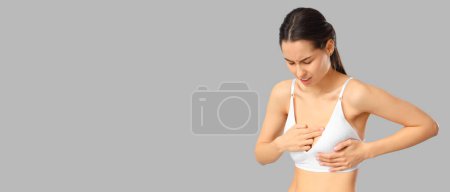 Foto de Mujer joven sintiendo dolor al tocar su pecho sobre fondo gris con espacio para el texto. Concepto de concienciación - Imagen libre de derechos