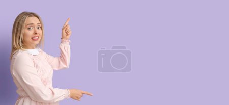 Photo for Embarrassed young woman pointing at something on lilac background with space for text - Royalty Free Image