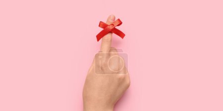 Female hand with red bow on index finger against pink background. Reminder concept