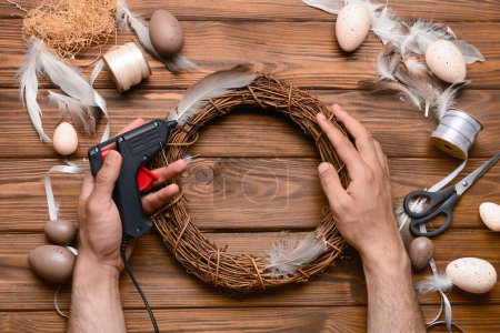 Téléchargez les photos : Homme créant une couronne de Pâques avec des plumes sur une table en bois marron - en image libre de droit