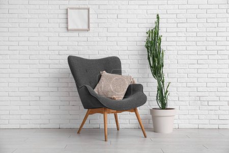 Big cactus with armchair near white brick wall in room