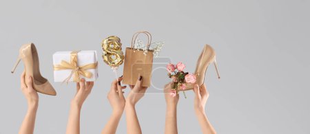 Manos femeninas con regalo, bolsa de compras y zapatos de tacón alto sobre fondo gris. Compras para el Día Internacional de la Mujer