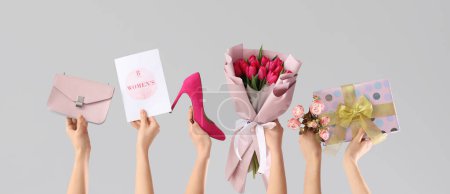 Weibliche Hände mit Tulpenstrauß, Geschenk, Schuh und Handtasche auf grauem Hintergrund. Einkaufen zum Internationalen Frauentag