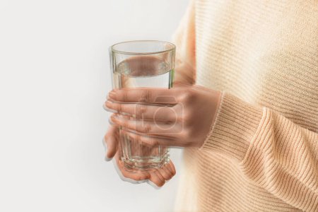 Photo for Woman holding glass of water in trembling hands on light background, closeup. Parkinson's Awareness Month - Royalty Free Image