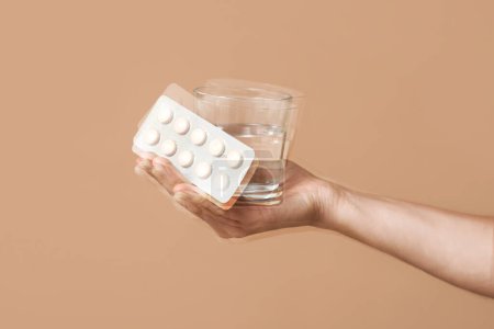 Photo for Trembling hand with glass of water and pills on beige background. Parkinson's Awareness Month - Royalty Free Image