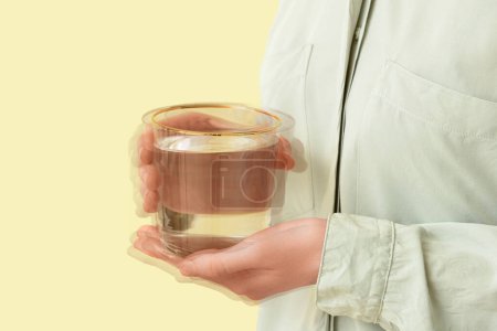 Photo for Woman holding glass of water in trembling hands on yellow background, closeup. Parkinson's Awareness Month - Royalty Free Image