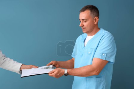 Mature doctor taking bribe from man on blue background