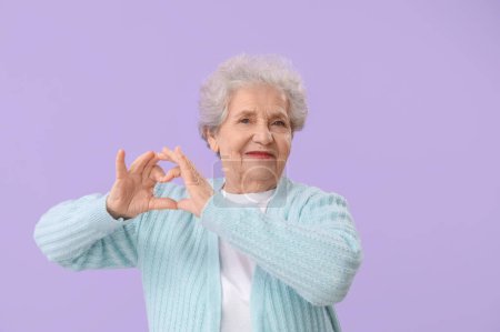 Femme âgée faisant c?ur avec ses mains sur fond lilas