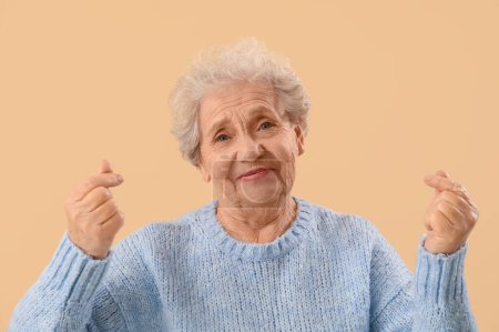 Femme âgée faisant coeur avec ses doigts sur fond beige